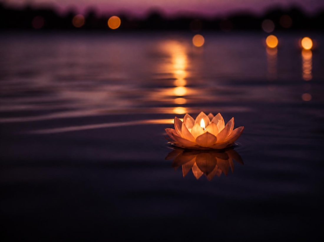 A lotus-shaped candle glowing on still water at dusk